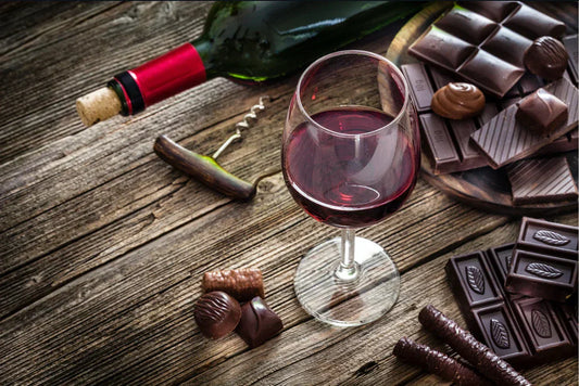 Red wine glass with assorted chocolate pieces and truffles on rustic wooden table, wine and chocolate pairing