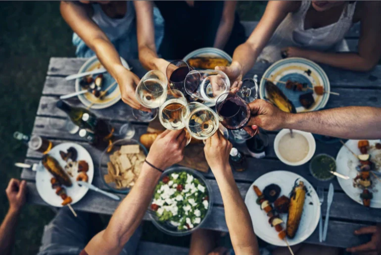Friends raising glasses of vegan red and white wine over an outdoor dinner table with shared plates, symbolising social wine drinking.