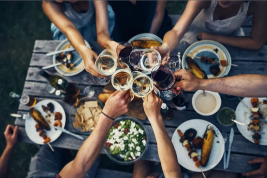 Friends raising glasses of vegan red and white wine over an outdoor dinner table with shared plates, symbolising social wine drinking.