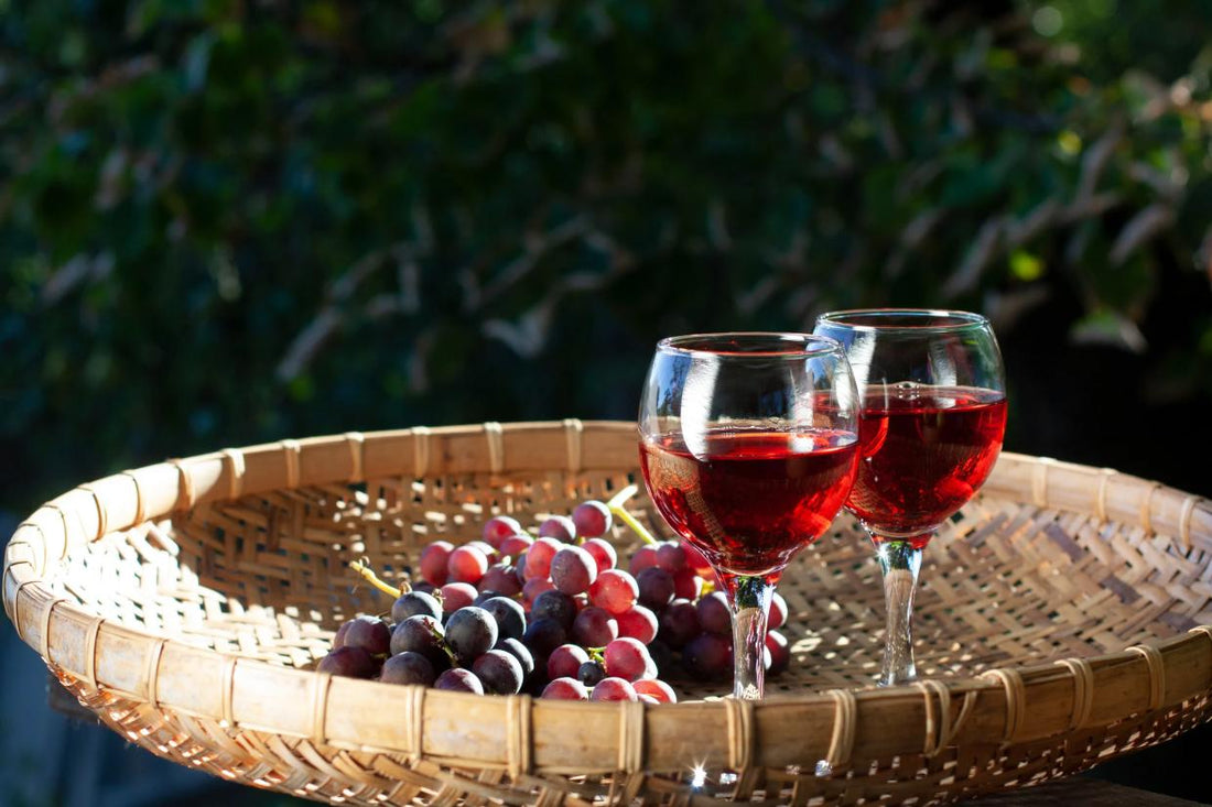 Two glasses of light red wine with fresh grapes in a basket outdoors.