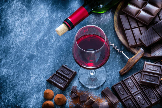 Glass of sweet red wine paired with dark chocolate bars and truffles on a rustic table.