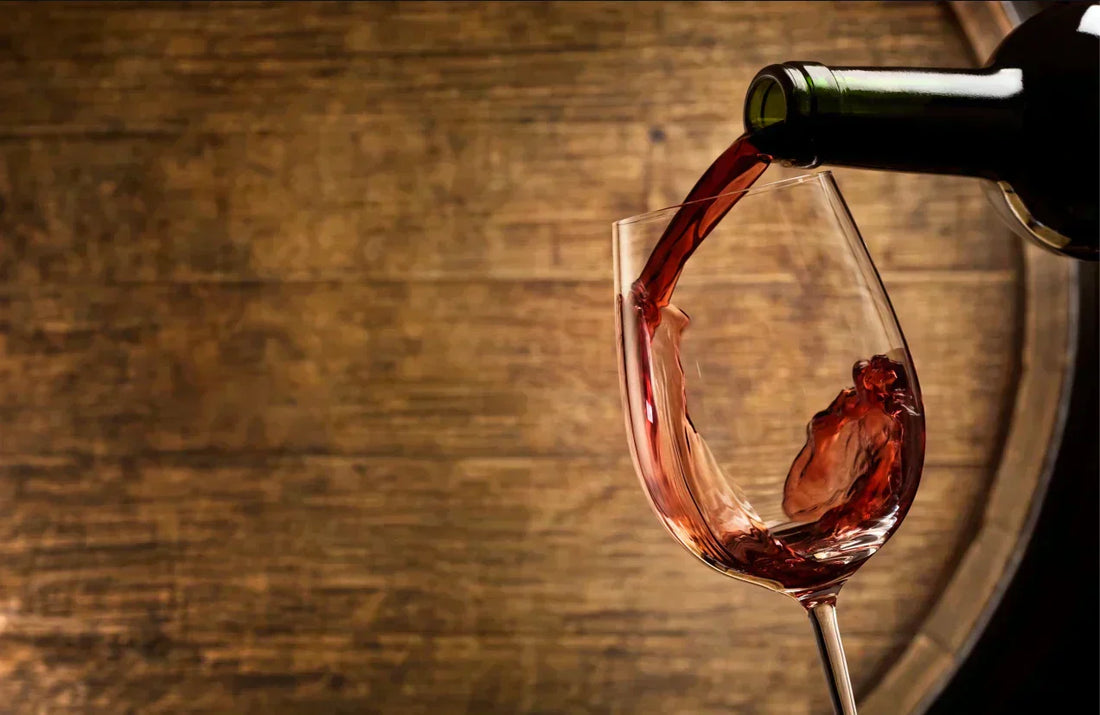 Red wine being poured into a glass in front of a wooden barrel, highlighting wine tannins