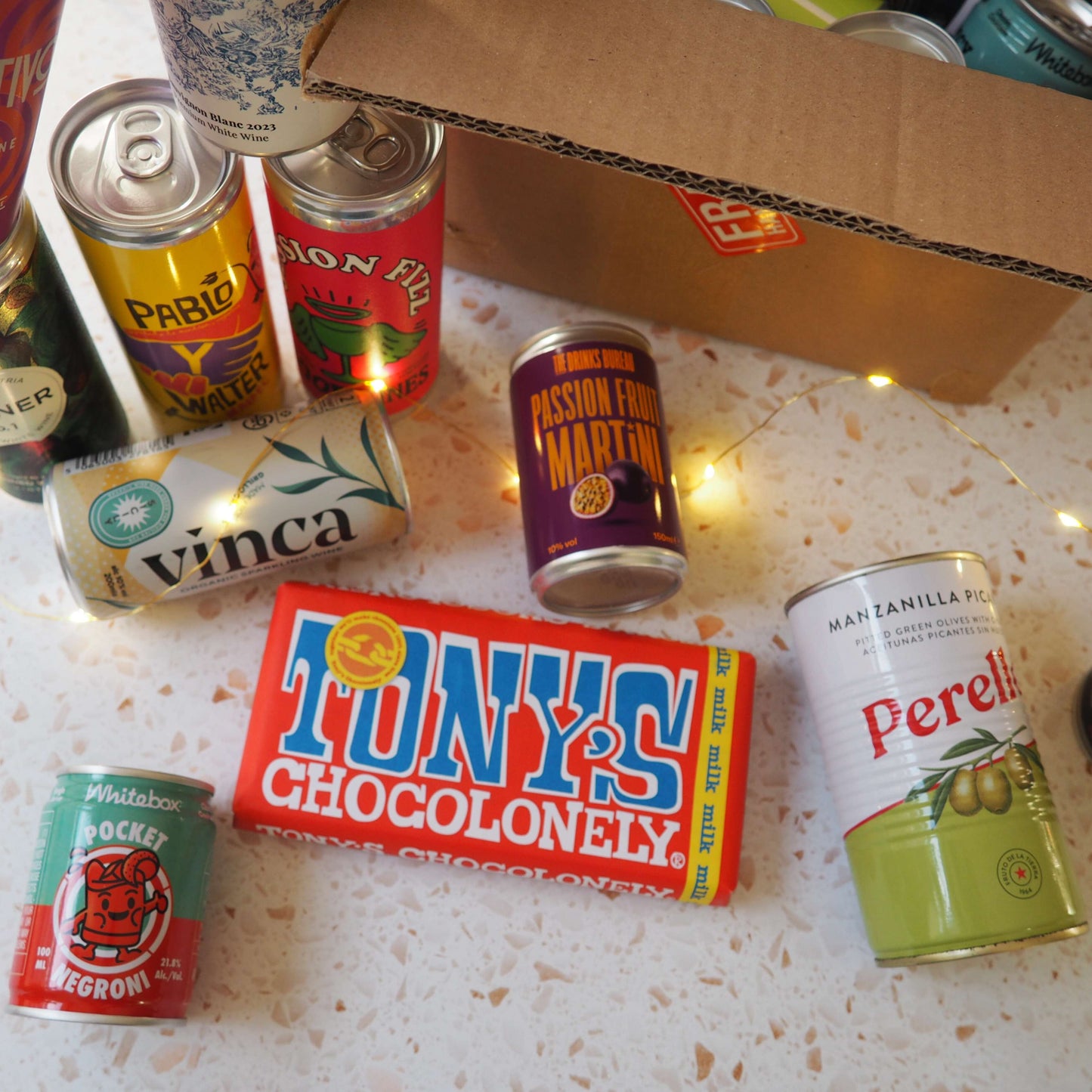 A gift including a selection of cans of wine, canned cocktails, olives and chocolate.